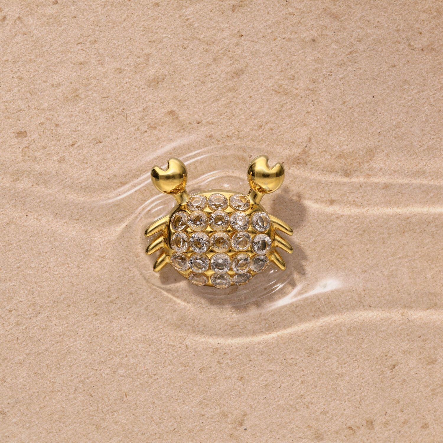 Goldener Push Fit Krabbenaufsatz Goldener Krabbenaufsatz mit Strasssteinen auf sandigem Hintergrund