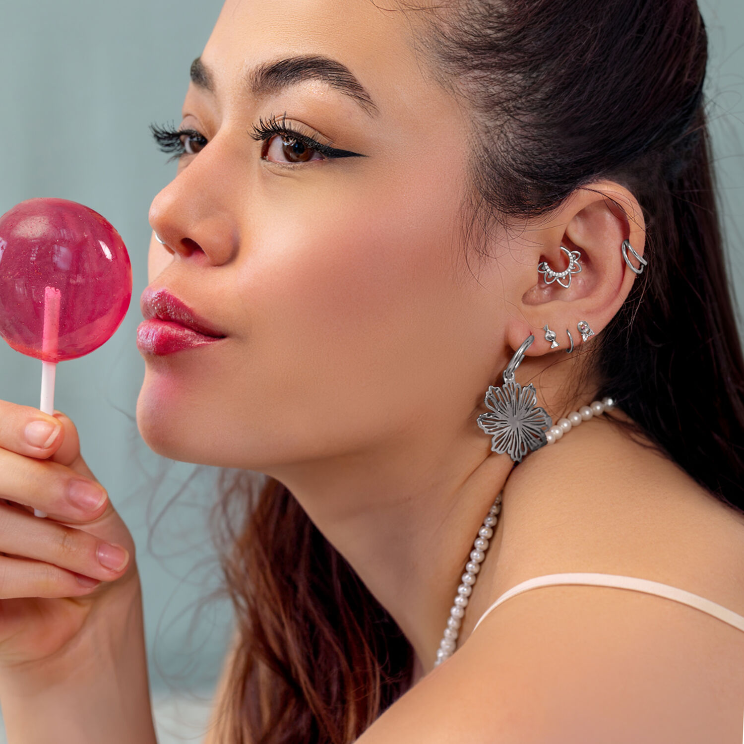 Silberne Ohrpiercings mit Lollipop Frau mit mehreren silbernen Ohrpiercings und einem rosa Lollipop, seitlich