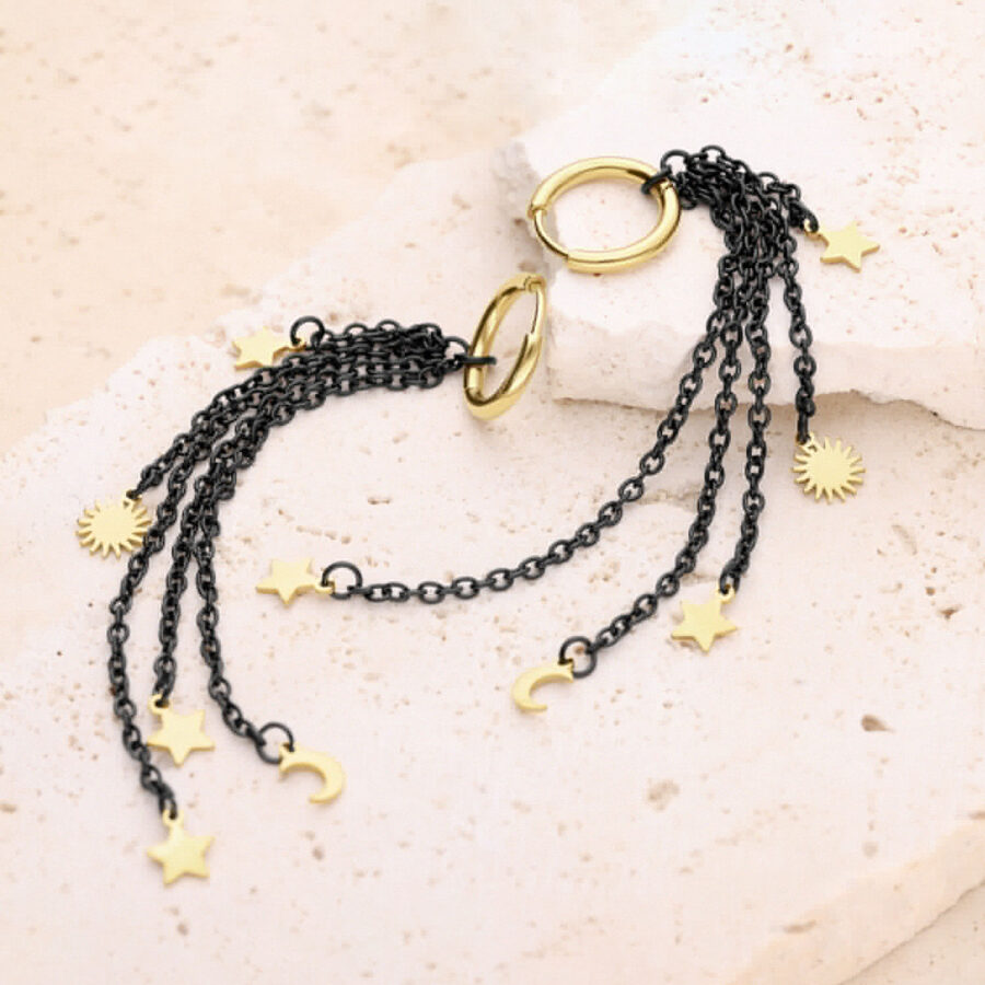Schwarze und goldene Ohrringe mit Stern- und Mondanhängern auf einem beigen Hintergrund