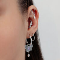 Silberne Ohrpiercings mit Kristallen Nahaufnahme eines Ohres mit mehreren silbernen Piercings, Kristallen und einem Schmetterlingsanhänger auf einem weißen Hintergrund.