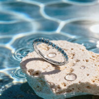 Türkisfarbener Kristallring auf Stein Türkisfarbener Kristallring auf einem hellen Stein am Rand eines Pools mit Sonnenlichtreflexionen