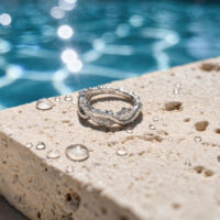 Weißgoldener Wave Clicker am Pool Weißgoldener Ring mit Kristallen auf Steinoberfläche, vor einem Pool