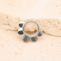 Silberner Half Flower Clicker aus Titan Silberner Half Flower Clicker vor einem beige Stein auf hellem Hintergrund