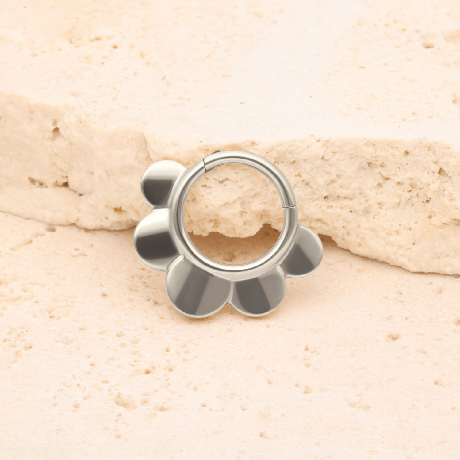 Silberner Half Flower Clicker aus Titan Silberner Half Flower Clicker vor einem beige Stein auf hellem Hintergrund