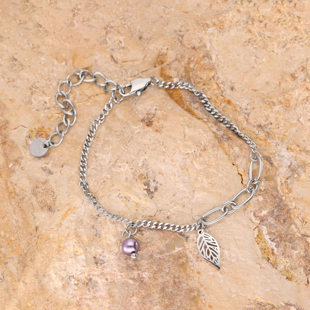 Feines silbernes Armband mit Blatt- und lila Perlenanhänger auf steinigem Hintergrund