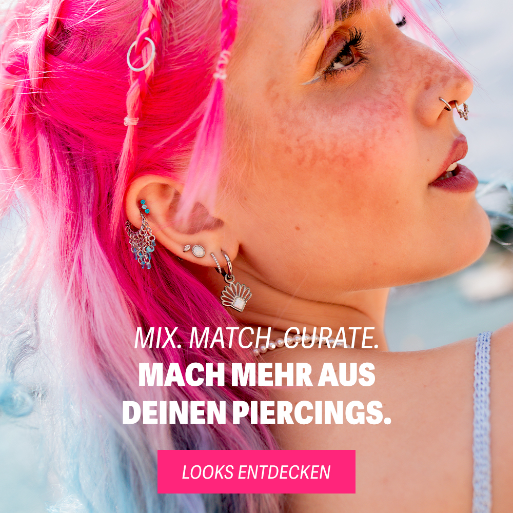Frau mit pinkem Haar, Herz-Sonnenbrille und verschiedenen Ohrpiercings am Strand