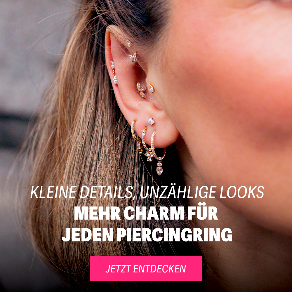Nahaufnahme von mehreren goldenen Piercingringen mit Glitzersteinen im Ohr einer Frau
