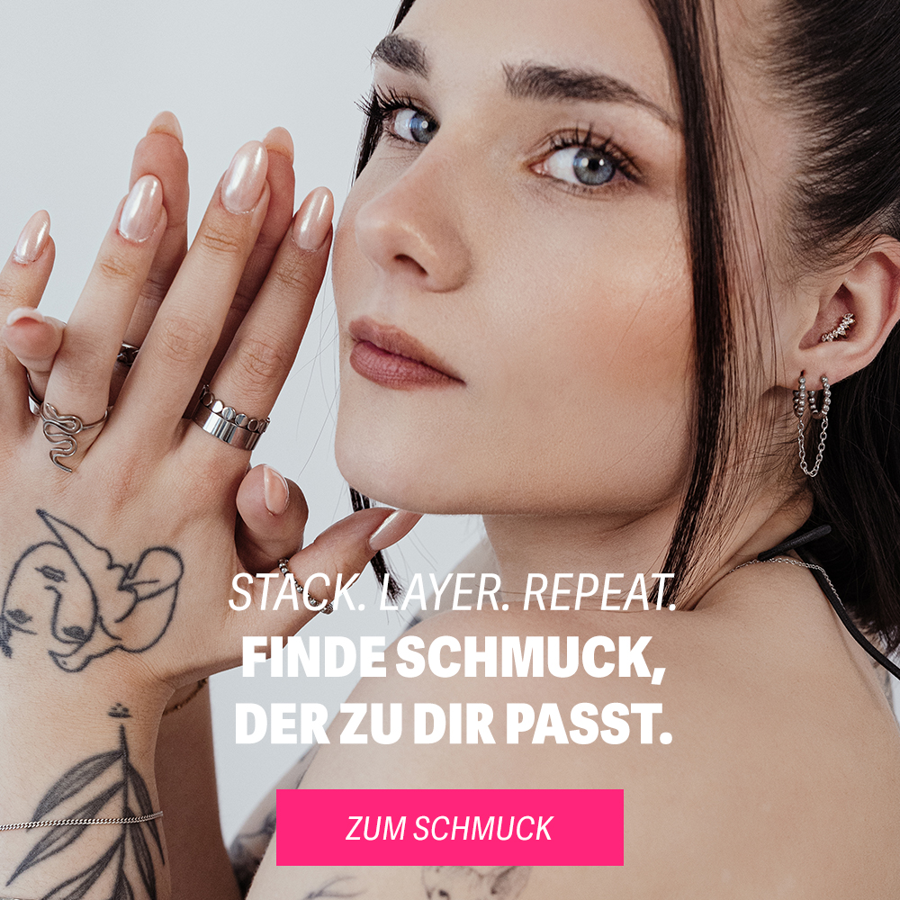 Junge Frau mit dunklem Haar trägt silberne Ohrringe und Ringe, zeigt eine tätowierte Hand auf weißem Hintergrund