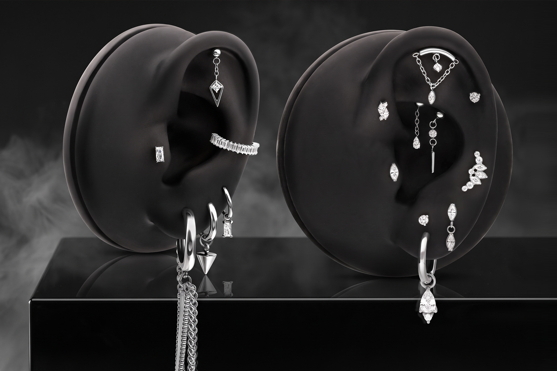 Zwei schwarze Ohrmodelle mit silbernen und glitzernden Piercings vor dunklem Hintergrund