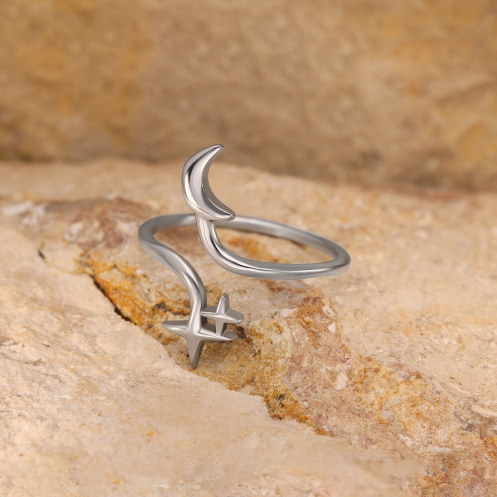 Silberner Ring mit Mond und Stern auf sandfarbenem Stein