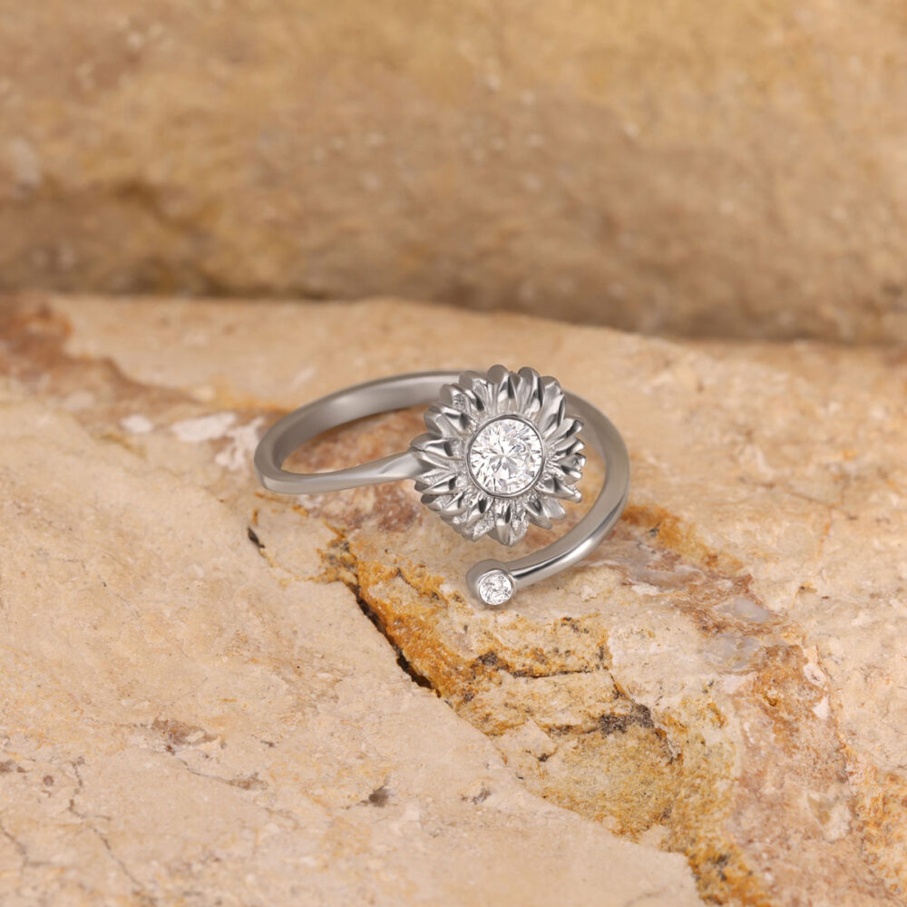 Silberner Ring mit Sonnenblumen-Design und Kristall auf steinigem Untergrund