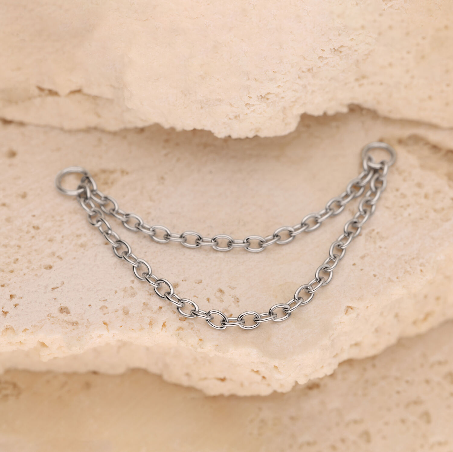 Silberne Doppelkette auf Stein Silberne Piercing-Doppelkette aus Chirurgenstahl auf beigem Stein