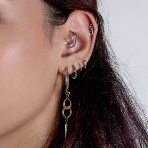 Nahaufnahme eines Ohres mit mehreren silbernen Piercings, darunter ein großer Anhänger und kleine Creolen auf weißem Hintergrund