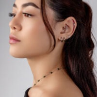 Silber Helix Piercing mit Kristallen Frau mit mehreren Silber-Piercings im Ohr, darunter ein kristallverzierter Helix-Aufsatz, vor grauem Hintergrund.