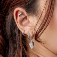 Nahaufnahme eines Ohrs mit mehreren silbernen Piercings und Kristallsteckern, Haar im Hintergrund