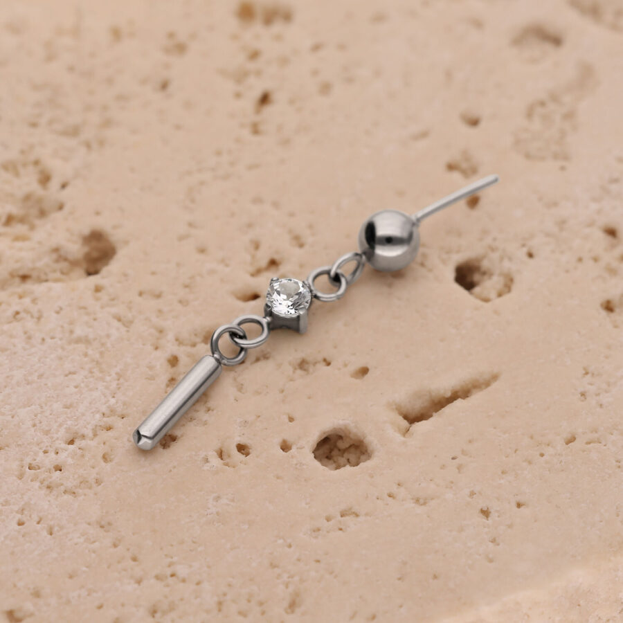 Silberner Piercingaufsatz mit rundem Kristall und kleinem Stab auf beige Struktur