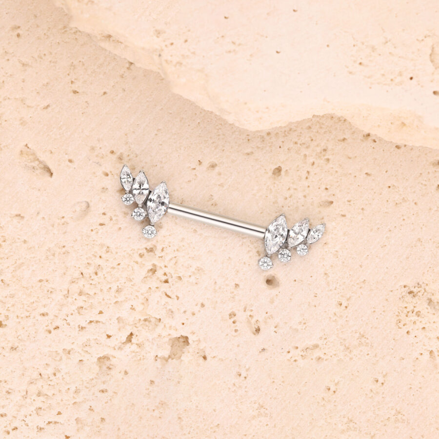 Silbernes Barbell mit Kristallflügeln auf beiger Steinoberfläche