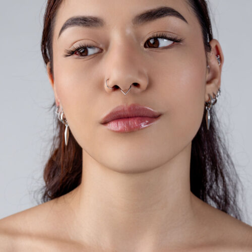 Frau mit silbernem Teardrop Clicker im Septum, neutraler Hintergrund
