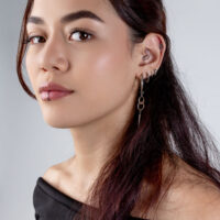 Frau mit einem Doppelring Clicker im Ohr und mehreren Piercings, vor grauem Hintergrund