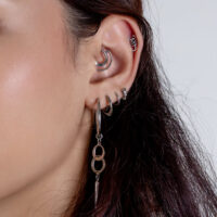 Nahaufnahme eines Ohrs mit mehreren silbernen Piercings und hängendem Schmuck