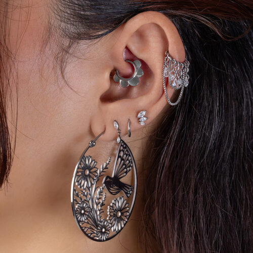 Großer, filigraner Ohrring in Blumenform an einem Ohr mit mehreren Piercings und einem silbernen Clicker.