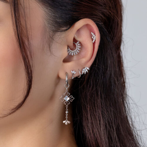 Nahaufnahme eines Ohrs mit mehreren silbernen Piercings und Kristallen.