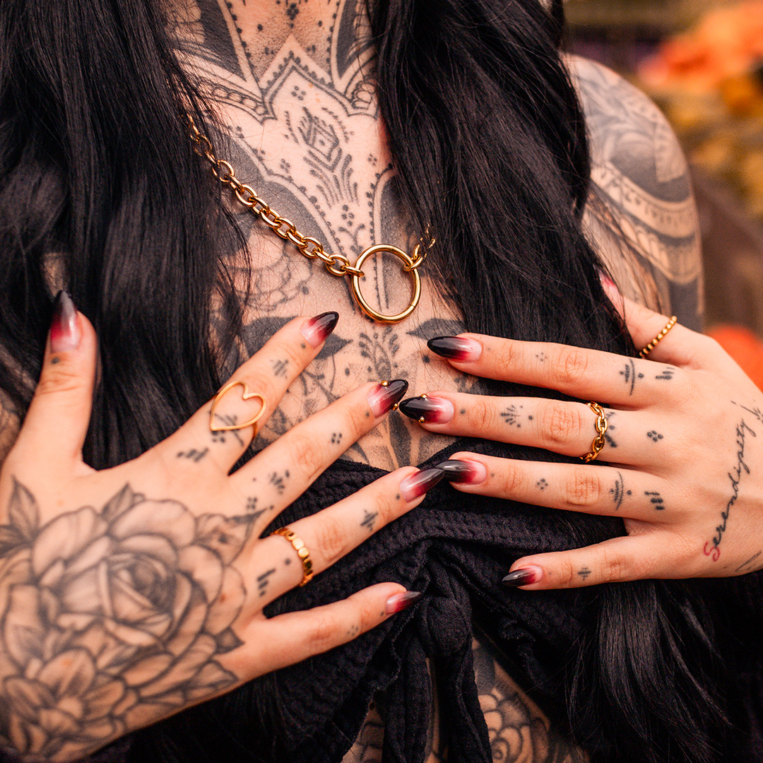 Frau mit schwarzen Haaren, goldener Kette, Tattoos und roten Nägeln