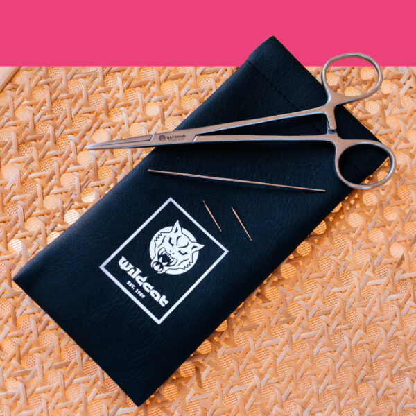Piercing-Werkzeugset mit schwarzer Tasche, Nadel und Klemme auf Korbgeflecht