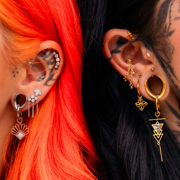 Zwei Ohren mit mehreren Piercings, bunte Anhänger und Ketten, rotes und schwarzes Haar