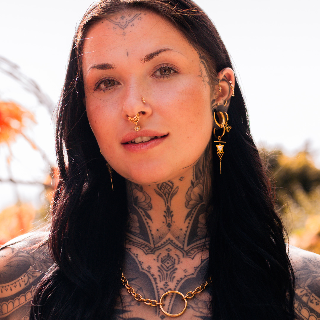Frau mit goldenen Ohrringen und Nasenring, Tattoos am Hals, im Freien