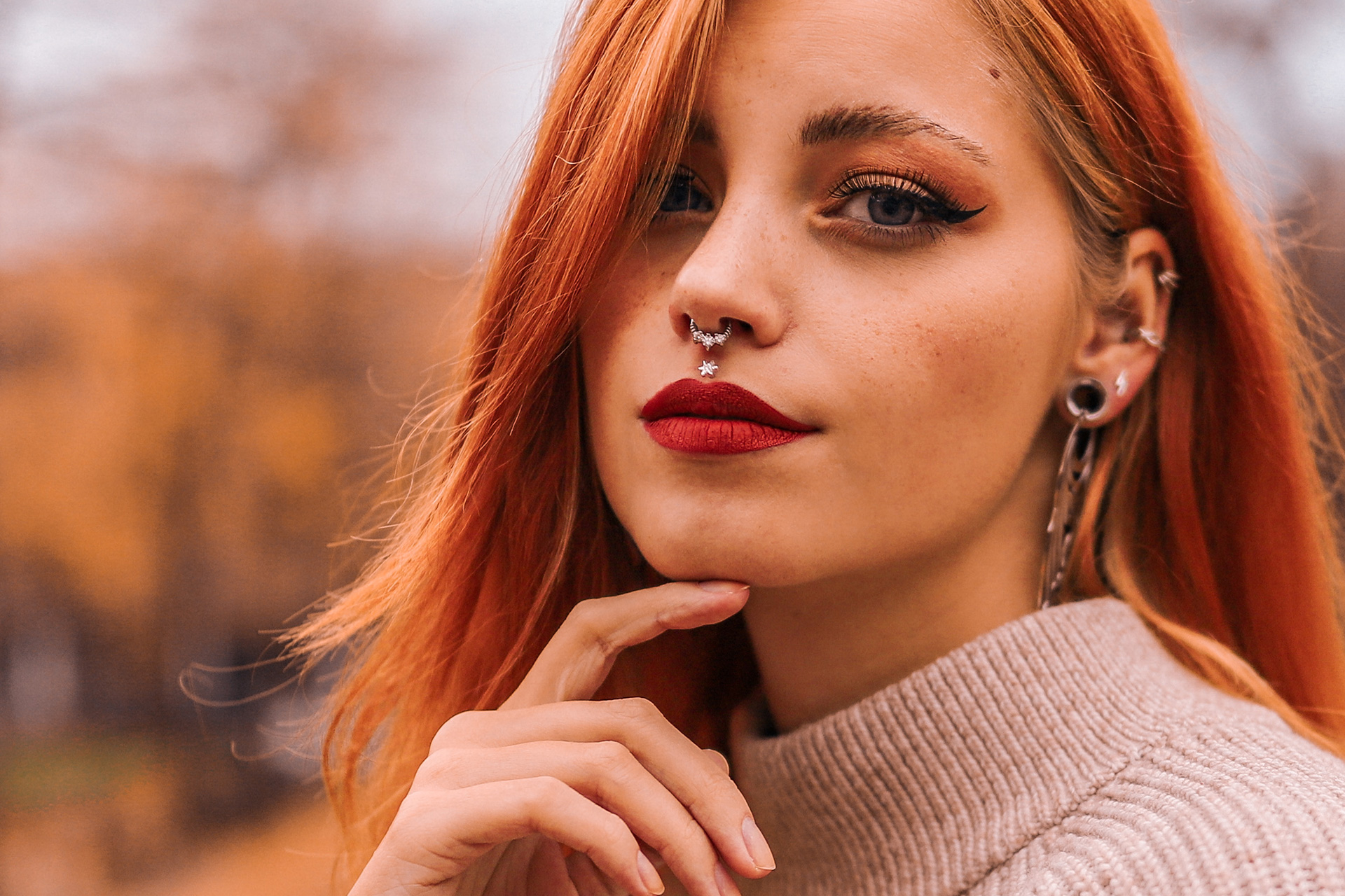 Junge Frau mit roten Haaren und rotem Lippenstift, Nasenpiercing, beige Pullover im Herbst