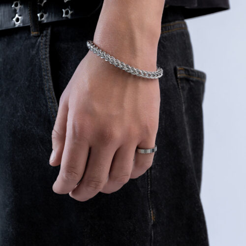 Person trägt ein silbernes Armband und einen Ring vor neutralem Hintergrund