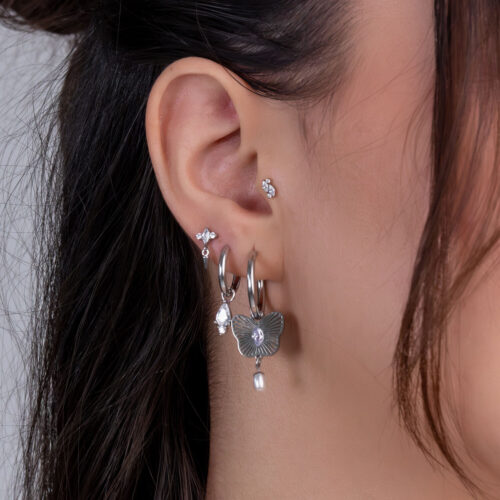Nahaufnahme eines Ohrs mit mehreren silbernen Piercings und klaren Kristallen auf einem hellen Hintergrund