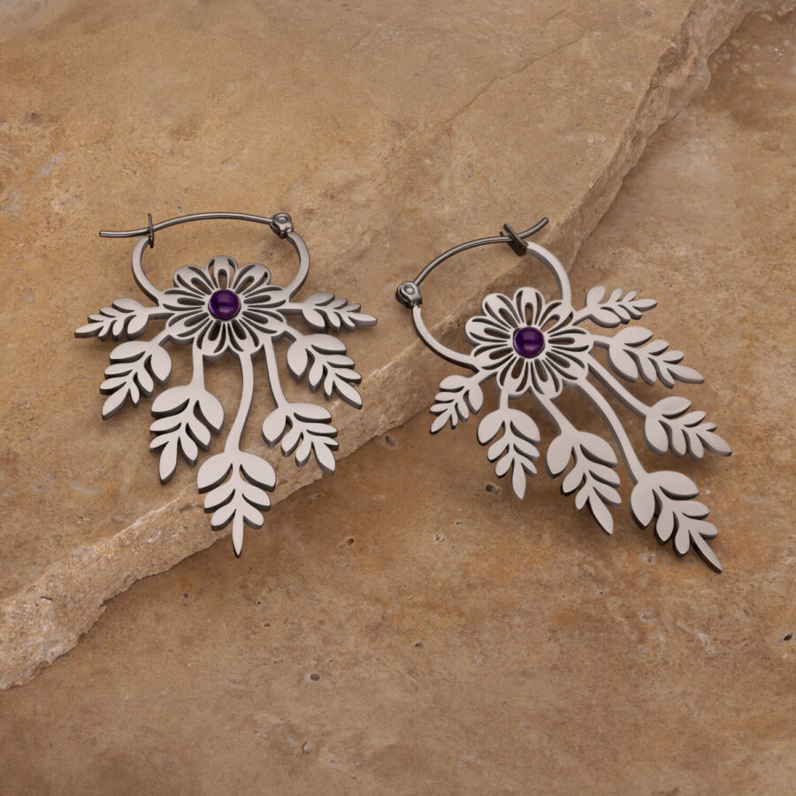Zwei florale Ohrringe mit Amethyst auf einem steinigen Hintergrund