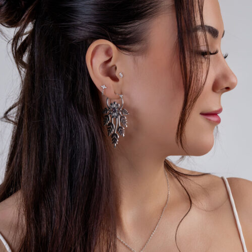 Frau mit langen Haaren trägt große silberne Blumen-Ohrringe und ein kleines Sternpiercing im Ohr, seitliches Profil